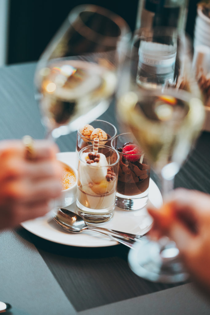 Zwei Hände stoßen mit champagner an. Dessert auf dem Tisch beim Brunch im Glashaus Restaurant